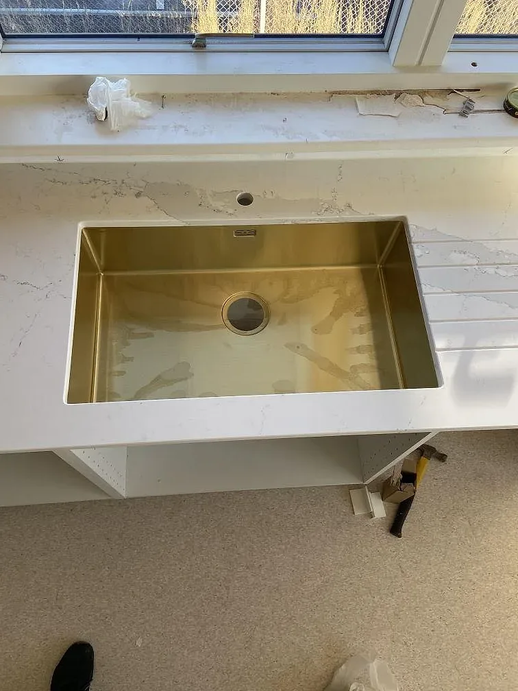Mässingsfärgad underlimmad diskho med separat borrat blandarhål i en vit Silestone Ethereal Dusk bänkskiva i ett kök i Oxie.