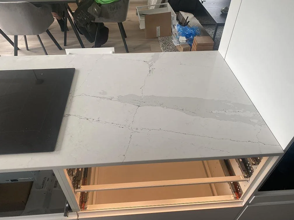 Köksö i Silestone Ethereal Dusk med induktionshäll och öppna lådor under montering, ljus komposit med grå ådring, Staffanstorp.