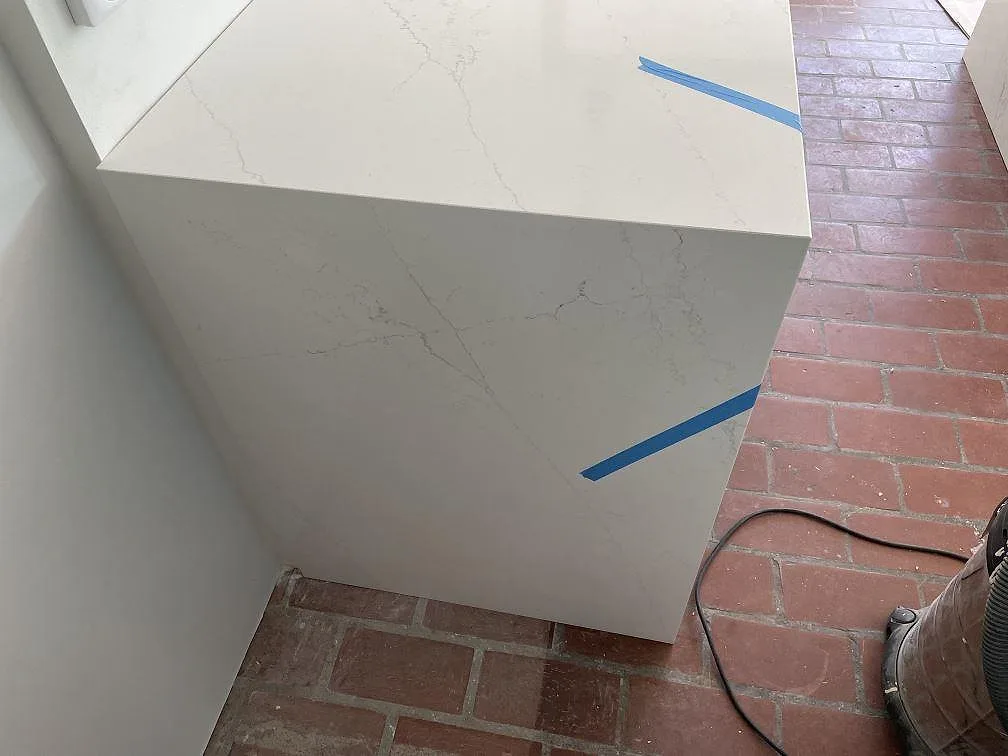 Detalj av köksöns gavel och polerad Silestone Ethereal Glow bänkskiva med blå fogtejp i Falsterbo.