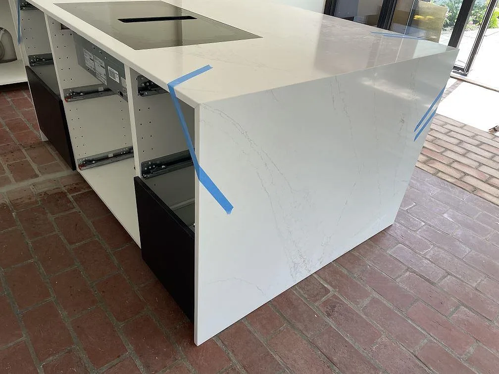 Köksö i polerad Silestone Ethereal Glow med diskhoöppning och vita stommar under montering i Falsterbo.