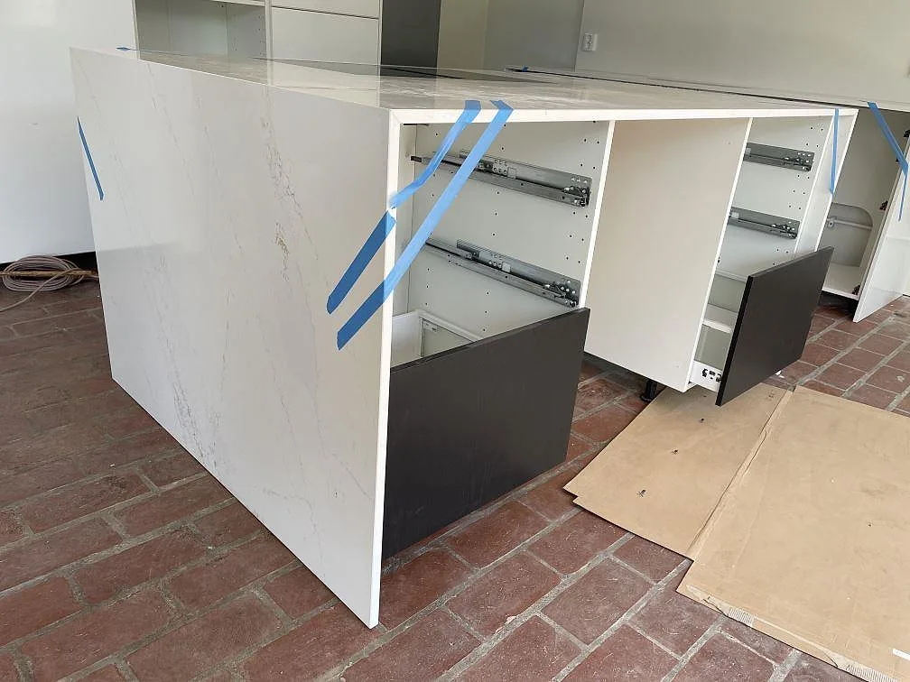 Polerad Silestone Ethereal Glow bänkskiva på köksö med öppna vita stommar och blå monteringstejp i Falsterbo.