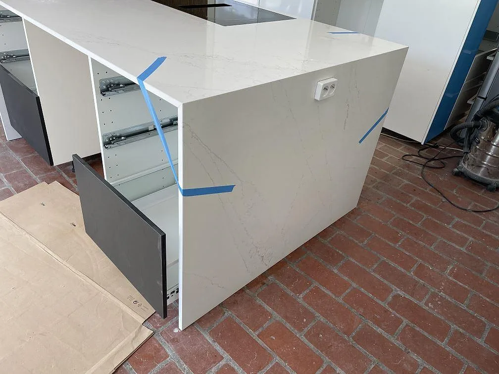Köksö i vit Silestone Ethereal Glow komposit, polerad, med öppna lådor och terrakottafärgat golv i Falsterbo.