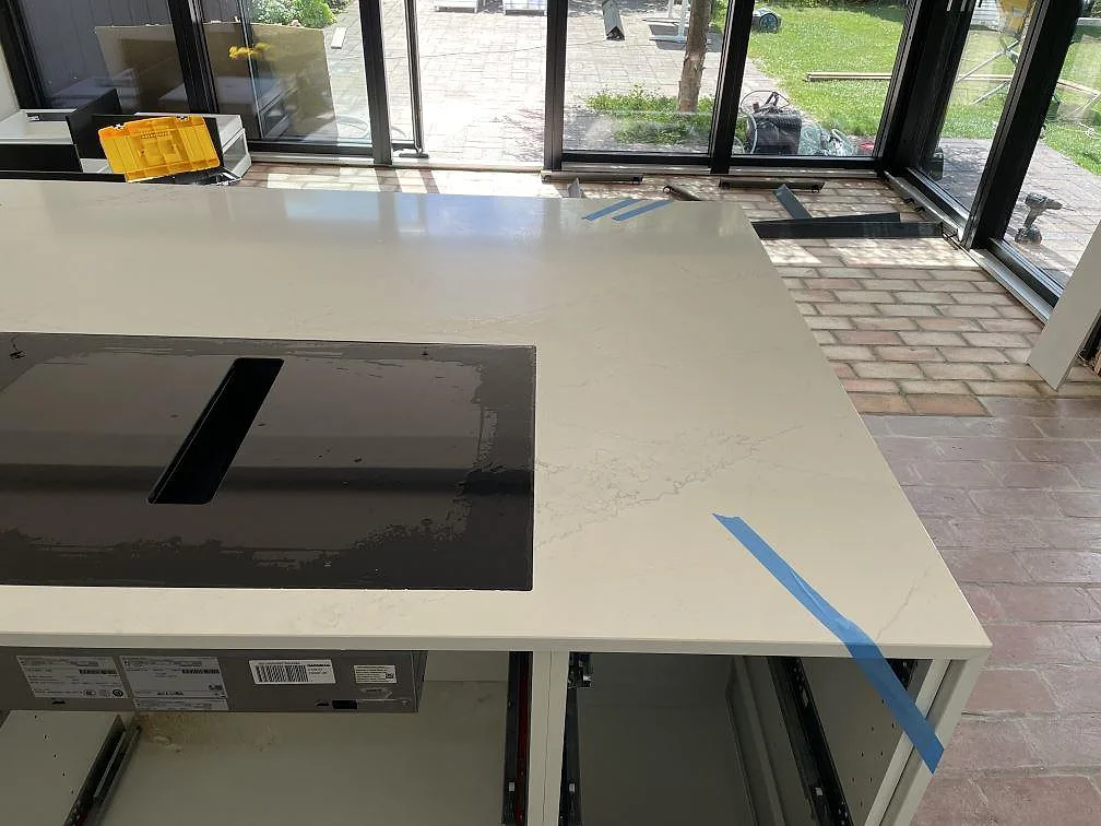 Köksbänkskiva i polerad Silestone Ethereal Glow, vit komposit, med svart häll på en stor köksö i Falsterbo.
