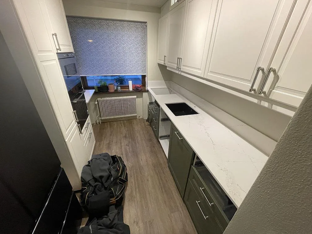 Köksbänkskiva i vit Silestone Ethereal Haze, polerad, sedd från dörröppningen med låg stänkkant och grön köksinredning i Helsingborg.