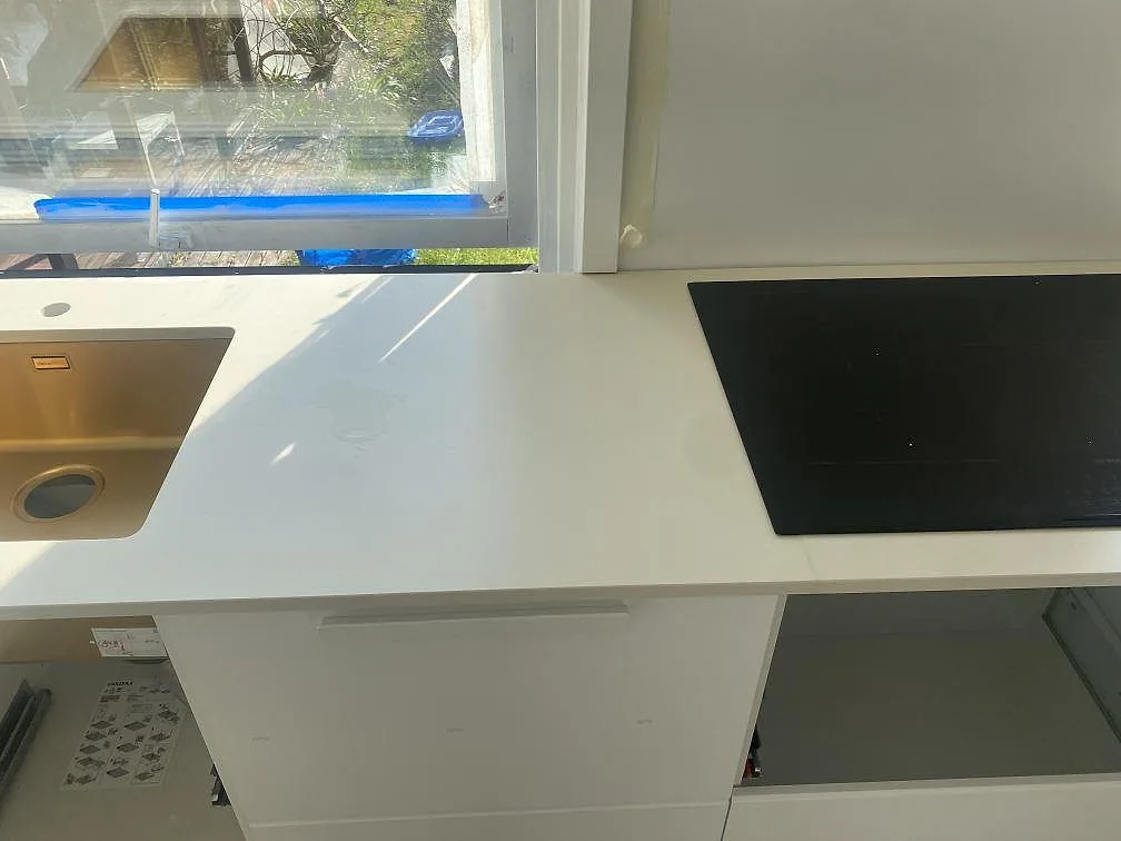 Köksbänkskiva i matt vit Silestone Faro White i Malmö, med underlimmad diskho i kopparton och infälld svart induktionshäll vid fönstret.