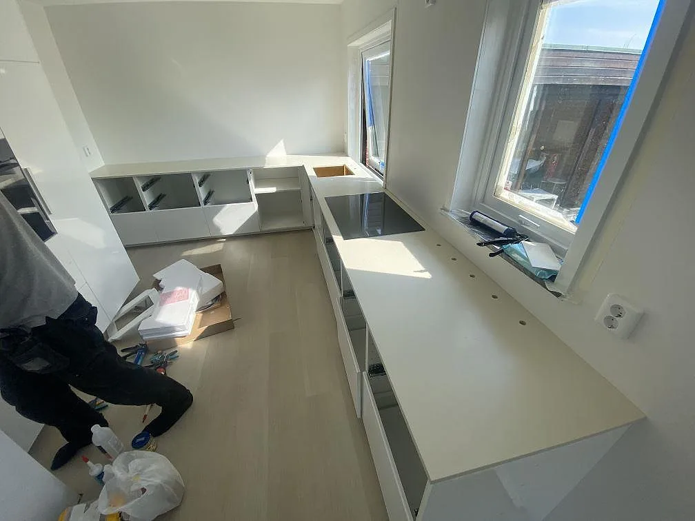 Vinklad köksuppställning med bänkskiva i matt vit Silestone Faro White i ett kök under montering i Malmö, med induktionshäll och öppna stommar.