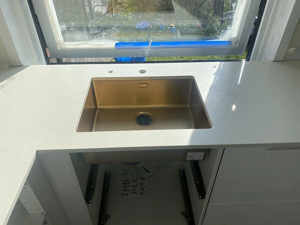 Underlimmad diskho i kopparton i en köksbänkskiva i matt vit Silestone Faro White vid fönstret i Malmö.
