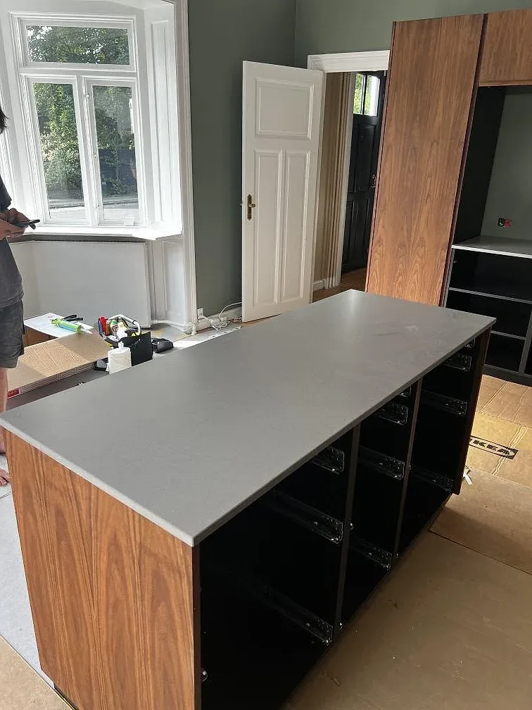 Köksö med matt kompositskiva i Silestone Gris Expo och valnötsfärgad träinredning under montering i Hellerup.