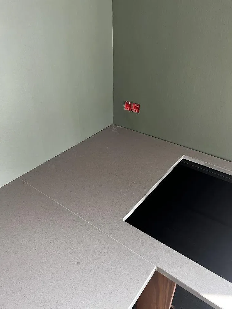 Detalj av hällöppning och skarv i matt Silestone Gris Expo komposit vid grön köksvägg i Hellerup.