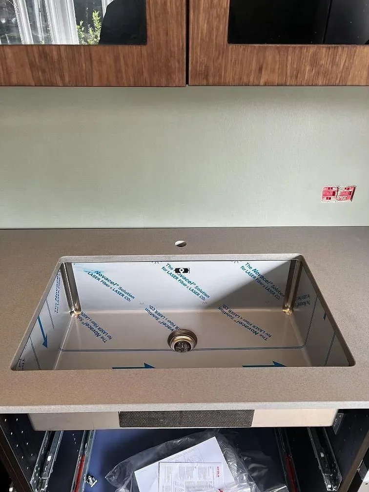 Underlimmad rostfri diskho i en matt Silestone Gris Expo bänkskiva med grön vägg och träskåp i Hellerup.