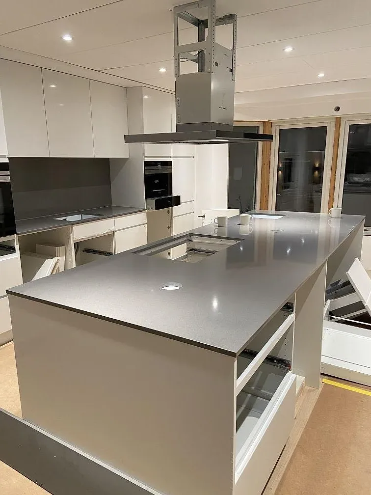 Köksbänkskiva i polerad grå Silestone Gris Expo i ett kök i Mölnlycke, vid eye-level under montering med vita köksstommar och stänkkant.