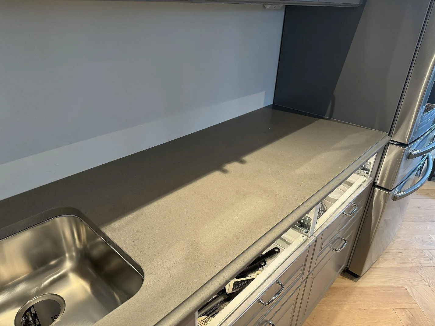 Lång bänkskiva i Silestone Gris Expo, 30 mm Mocka, med rostfri ho, uppvikt stänkkant och kyl vid sidan i Sölvesborg.