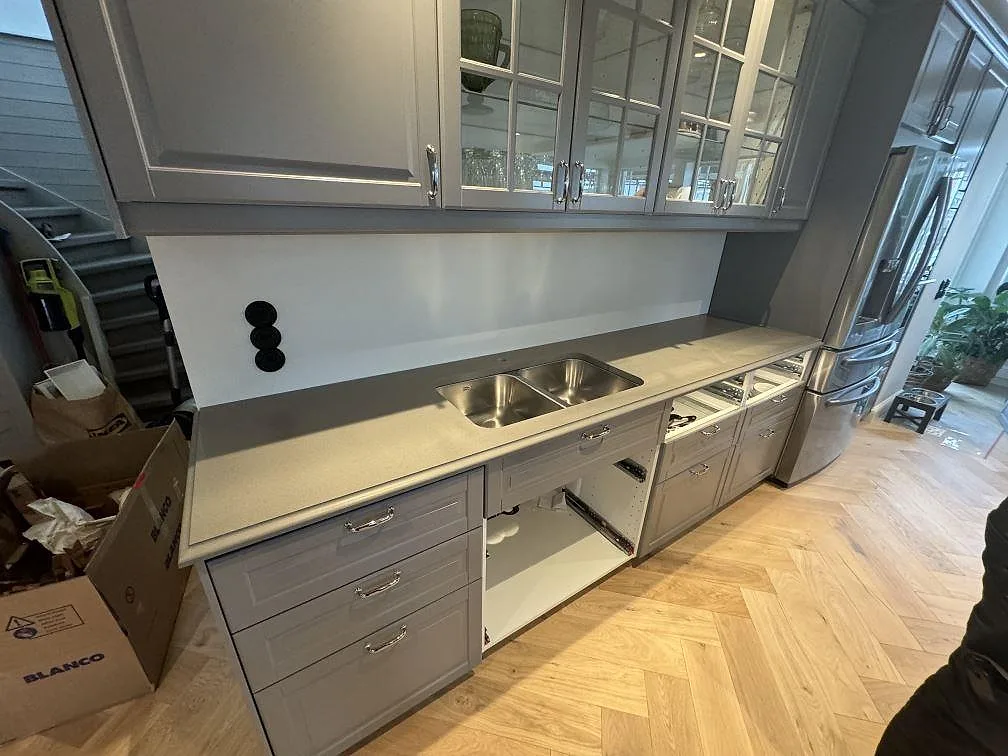 Bred vy av kök i Sölvesborg med köksbänkskiva i Silestone Gris Expo, Mocka-yta, rostfri dubbelho och ljust fiskbensgolv.