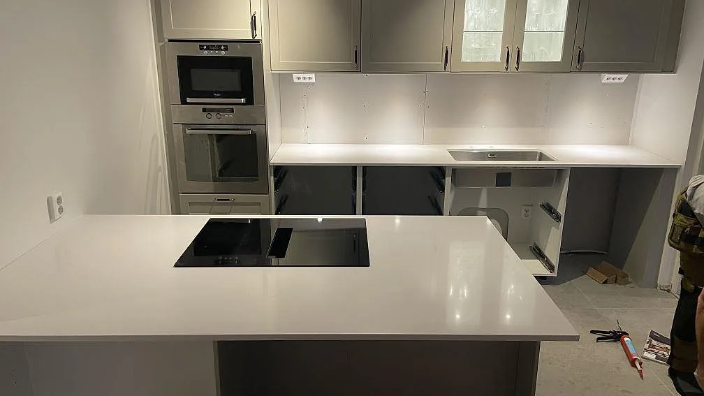 Köksbänkskiva i vit Silestone Iconic White, polerad, med köksö och induktionshäll samt underlimmad rostfri diskho i ett kök under montering i Vellinge.