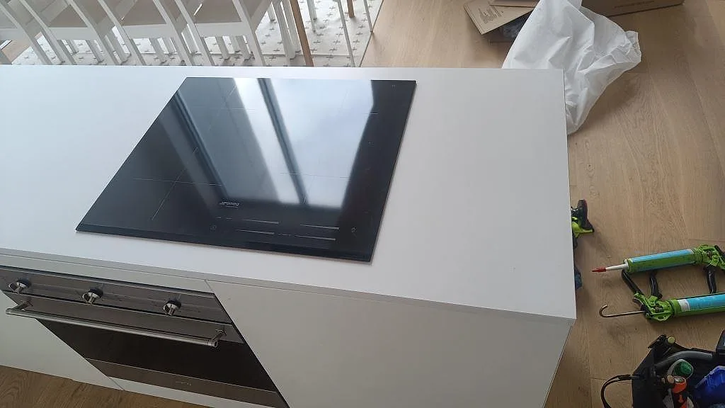 Detalj av infälld induktionshäll i en vit köksbänkskiva av Silestone Iconic White med matt Mocka-yta i Ystad.