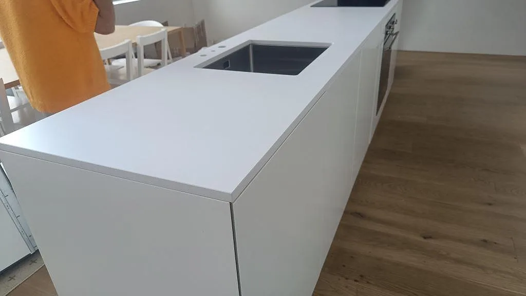 Köksö i vit Silestone Iconic White med matt Mocka-yta, underlimmad rostfri diskho och infälld häll under montering i Ystad.