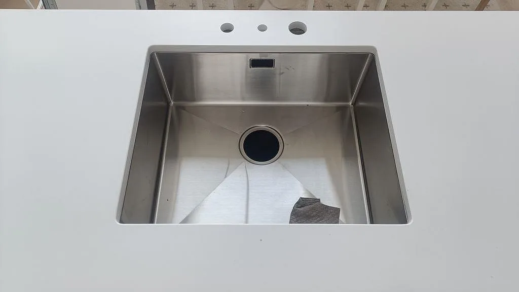 Närbild på underlimmad rostfri diskho i vit Silestone Iconic White, matt Mocka, med hål för blandare i Ystad.