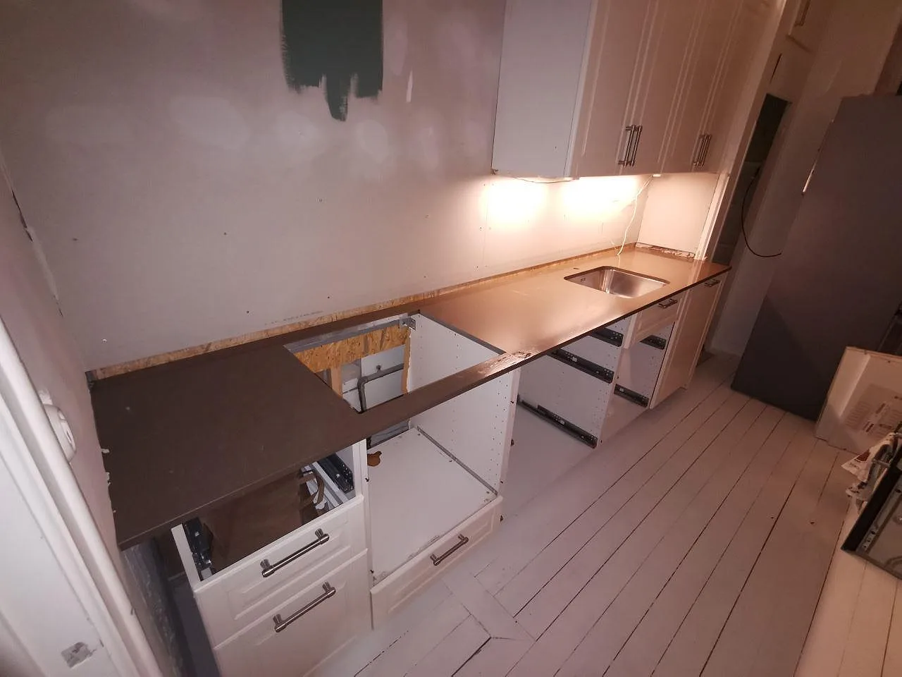 Köksbänkskiva i Silestone Iron Bark, polerad gråbrun kvartskomposit, monterad i en lång köksrad med underlimmad rostfri diskho under montering i ett kök i Malmö.