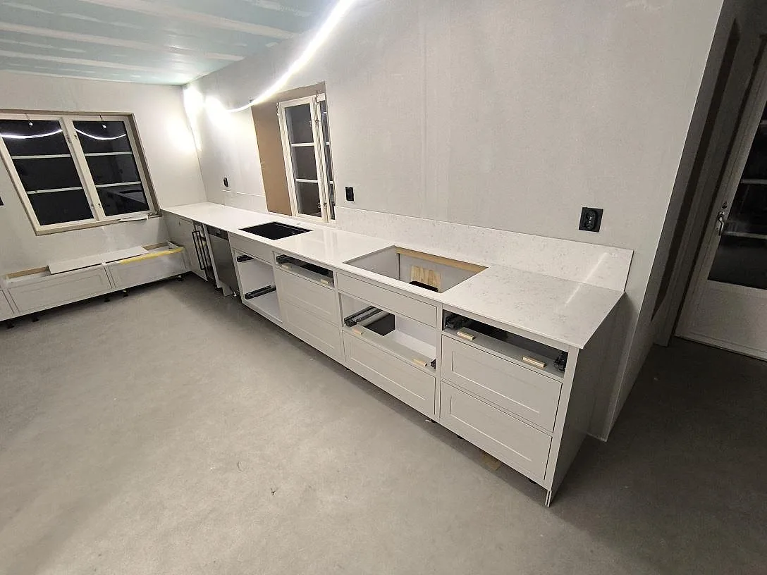 Rak köksbänkskiva i vit Silestone Lagoon, polerad kvartskomposit, med uppvikt stänkskydd, svart diskho och hällurtag i ett kök under montering i Avesta.