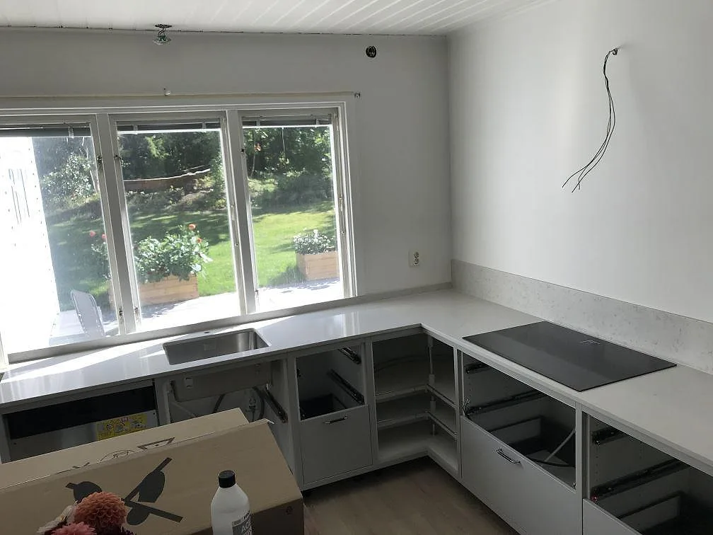 Köksbänkskiva i ljus Silestone Lagoon, polerad, i ett vinklat kök i Brämhult med underlimmad rostfri diskho och infälld induktionshäll under montering.