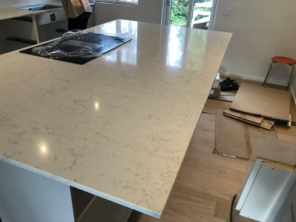 Polerad köksö i Silestone Lagoon med urtag för spishäll och utsikt mot trädgården i ett kök i Falsterbo.