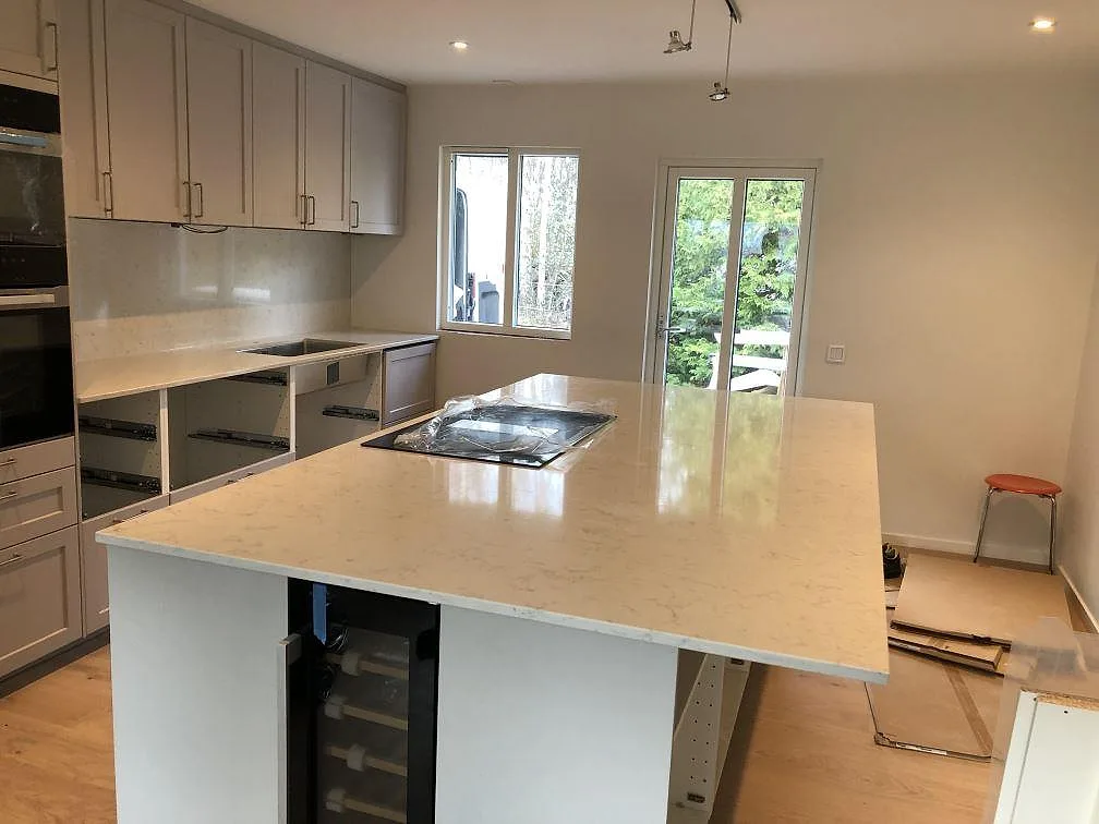Köksbänkskiva i vit Silestone Lagoon, polerad, på köksö och perimeterbänk med stänkskydd i ett kök under montering i Falsterbo.