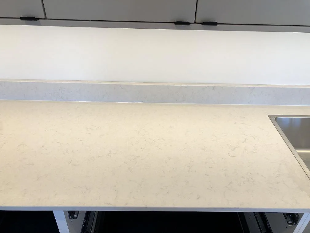 Lång köksbänk i creme Silestone Lagoon med låg uppvikt stänkkant och rostfri diskho i ett kök i Fjälkinge.