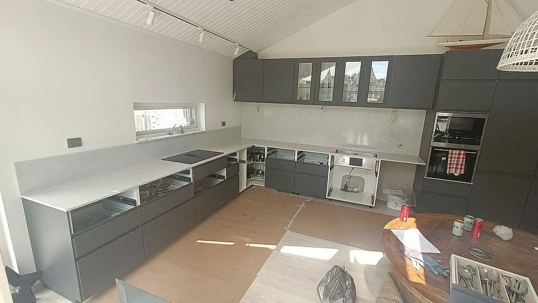 Köksbänkskiva i ljus Silestone Lagoon, polerad, monterad i ett L-format kök i Höllviken med infälld induktionshäll under installation.