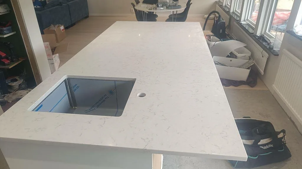 Lång köksö i polerad Silestone Lagoon med underlimmad diskho och ljus grå ådring i ett kök i Höllviken.
