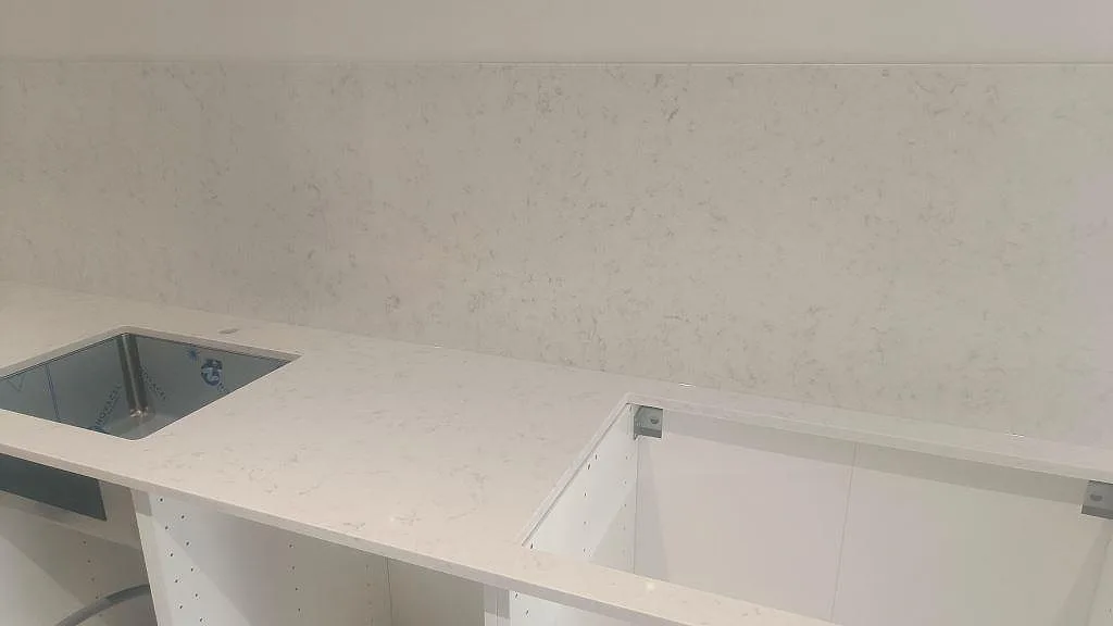 Väggbänk i polerad Silestone Lagoon med underlimmad diskho, ljusa stommar och stänkskydd i samma sten i Höllviken.