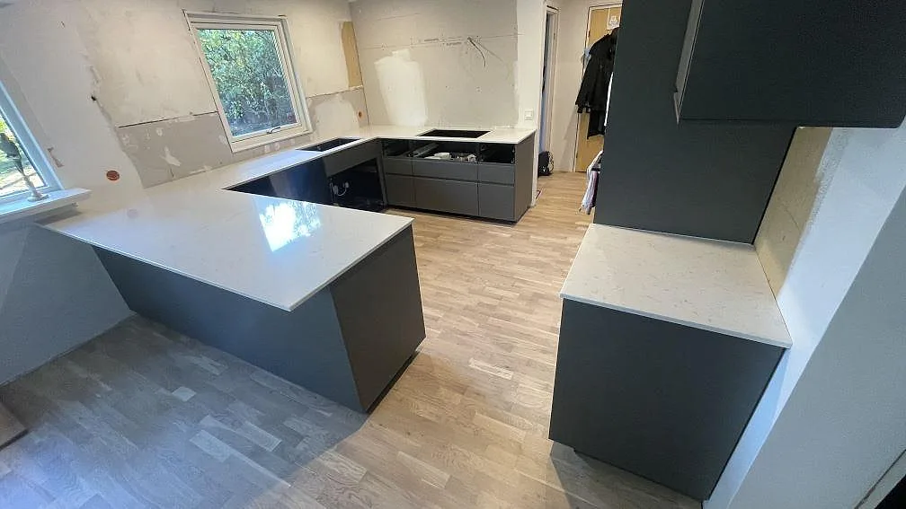 Köksbänkskivor och köksö i ljus polerad Silestone Lagoon kompositsten i ett kök under montering i Hörby.