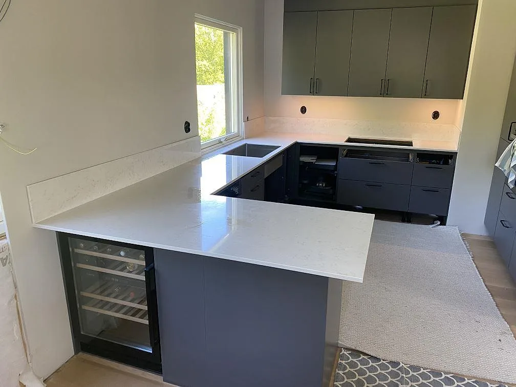 Köksbänkskiva i polerad Silestone Lagoon, ljus kvartskomposit med grå ådring, monterad som L-formad bänk och framskjutande arbetsyta i ett kök i Hovås.