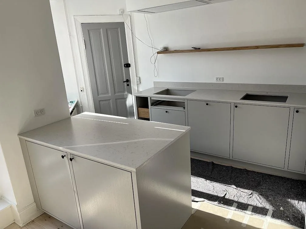 Köksbänkskiva och köksö i polerad Silestone Lagoon, ljus crèmevit kvartskomposit, monterad i ett kök i København med urtag för häll och underlimmad diskho i bänkraden längs väggen.