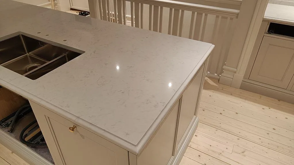 Köksö med polerad Silestone Lagoon komposit, vit skåpinredning och underlimmad rostfri diskho i Lekeryd.