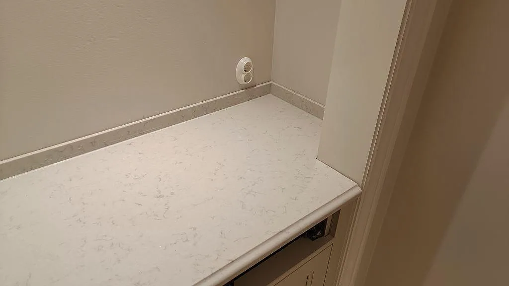 Sidobänk med låg stänkkant i polerad Silestone Lagoon komposit intill vägguttag i Lekeryd.