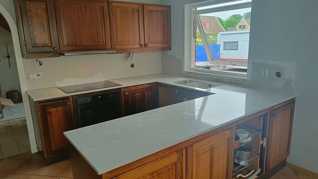Köksbänkskiva i krämvit Silestone Lagoon, polerad, i ett U-format kök med halvö, induktionshäll och underlimmad rostfri diskho i Löberöd.