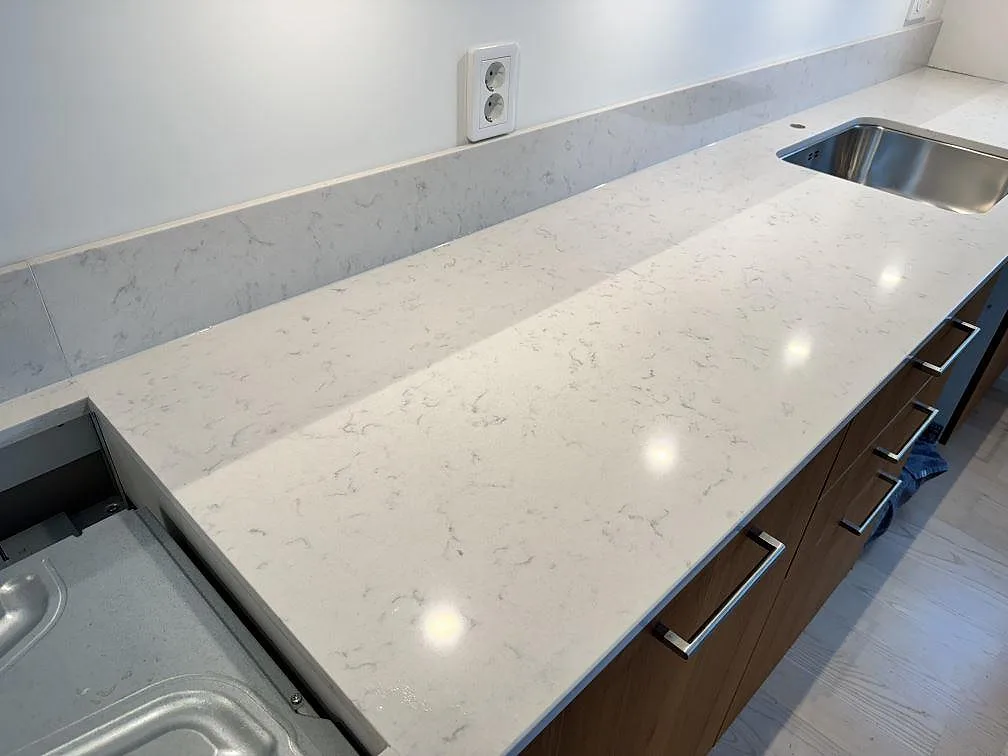 Lång köksbänkskiva i polerad Silestone Lagoon med grå ådring, träinredning och rostfri diskho i Lomma.