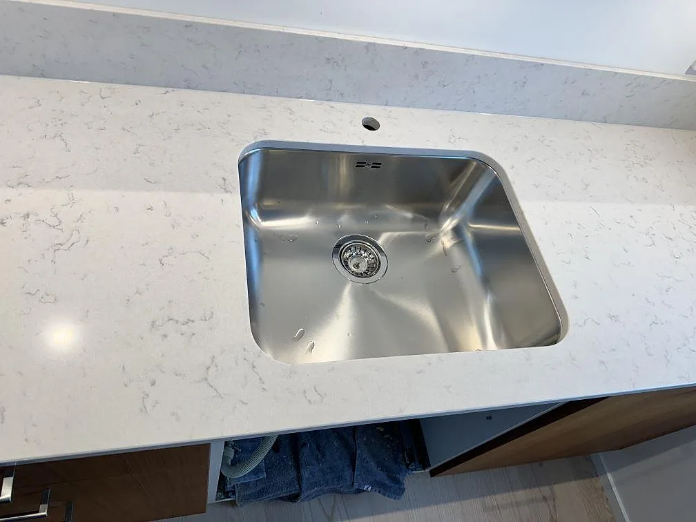 Rostfri diskho monterad under en vit köksbänkskiva i polerad Silestone Lagoon i Lomma.