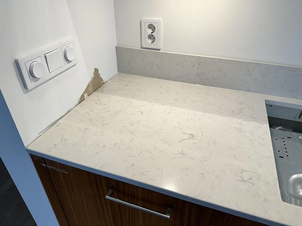 Detalj av ljus Silestone Lagoon som köksbänkskiva med uppvikt stänkskydd och träluckor i Lomma.