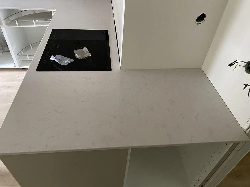 Köksbänkskiva i krämvit Silestone Lagoon, polerad, med svart induktionshäll infälld i köksön i ett kök under montering i Malmö.