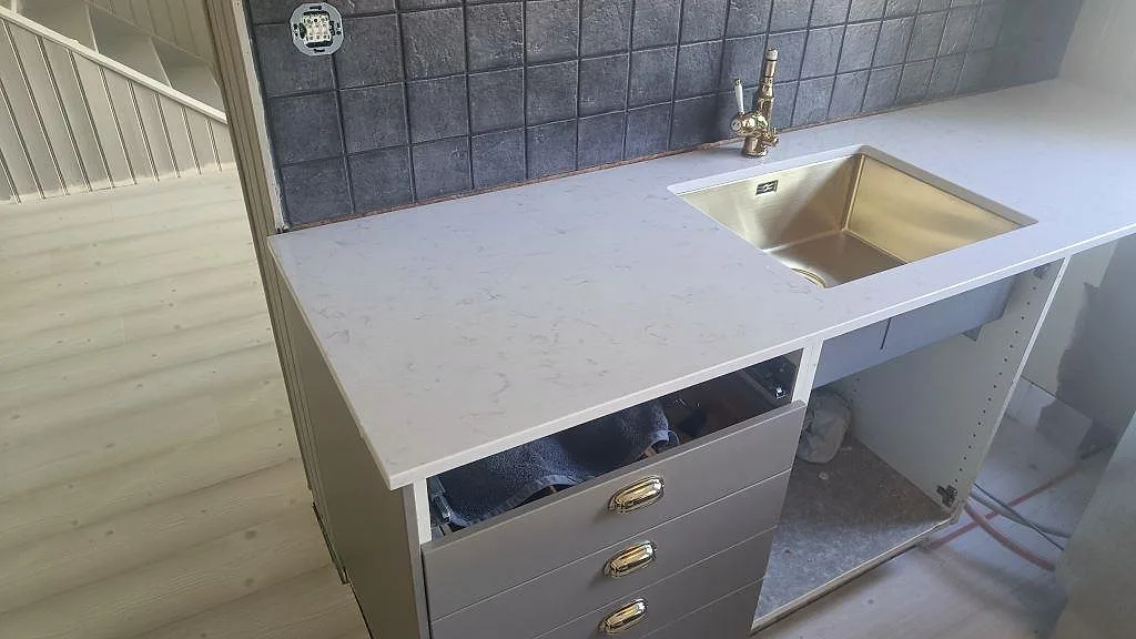Polerad kompositbänkskiva i Silestone Lagoon med underlimmad mässingsfärgad diskho och grått kakel i kök i Mariestad.