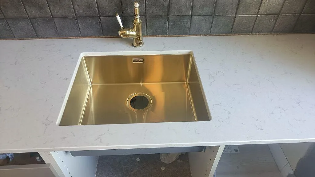 Närbild på underlimmad mässingsfärgad diskho i polerad Silestone Lagoon med ljus grå ådring i Mariestad.