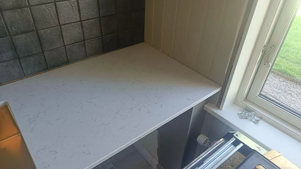 Sidobänk i polerad Silestone Lagoon, 20 mm, intill grått kakel och fönster i kök i Mariestad.