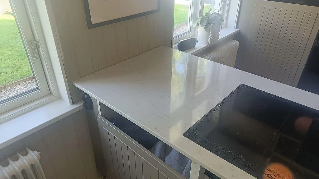 Köksö med svart häll i polerad Silestone Lagoon och ljus stenkomposit i ett kök i Mariestad.