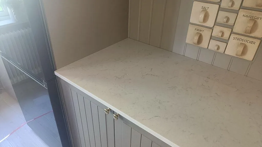 Serveringsbänk i polerad Silestone Lagoon med grå ådring och pärlspontad köksinredning i Mariestad.
