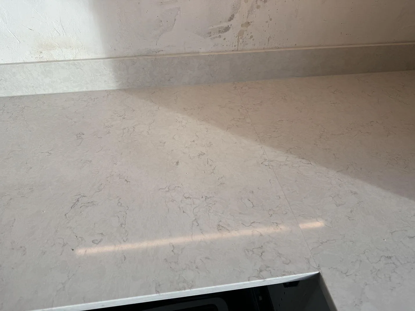 Närbild av polerad Silestone Lagoon med mjuk grå ådring och matchande stänkskydd i ett kök i Pixbo.