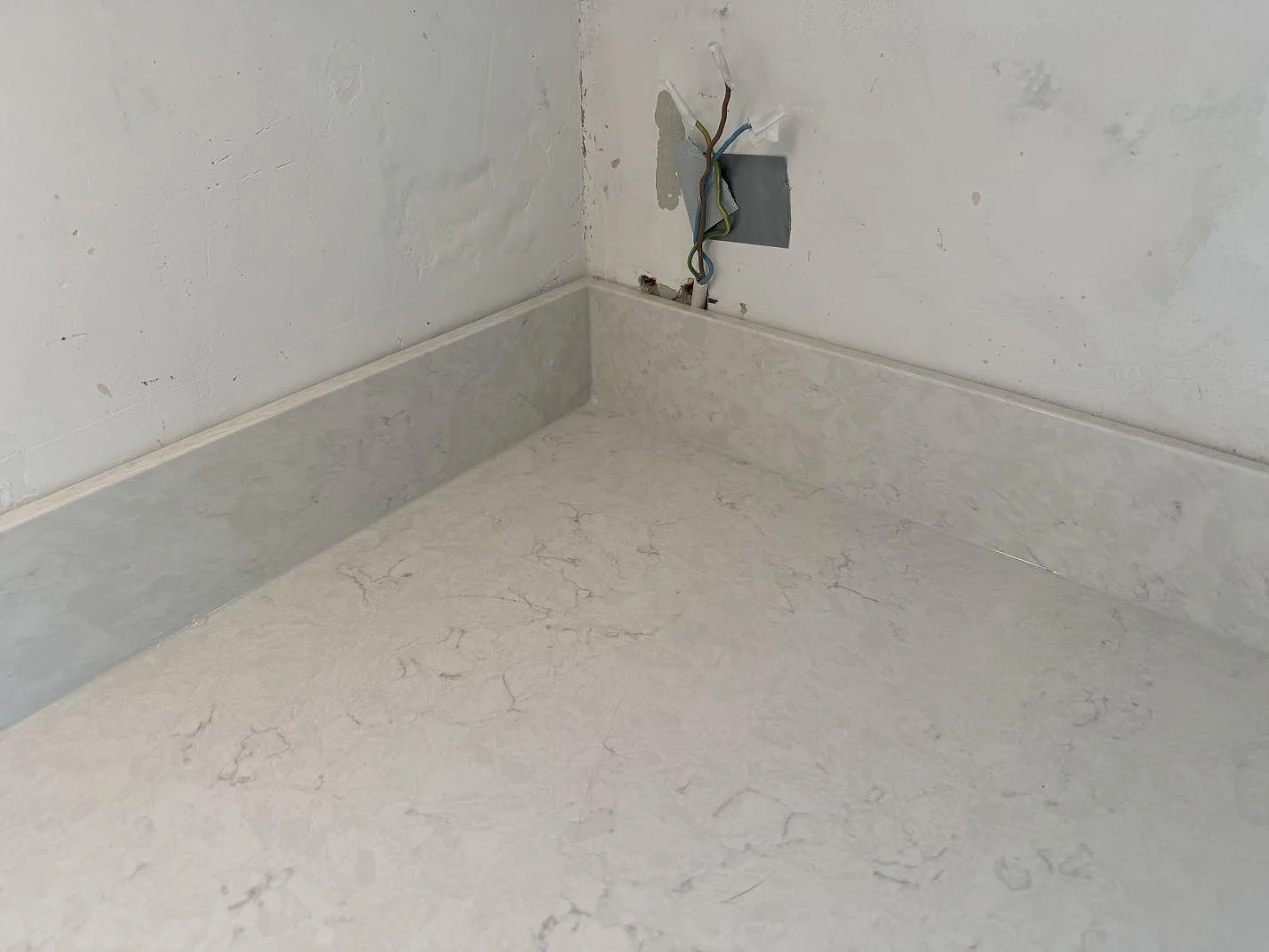 Hörn med polerad Silestone Lagoon, ljus köksbänkskiva och låg stänkkant under eluttag i Pixbo.