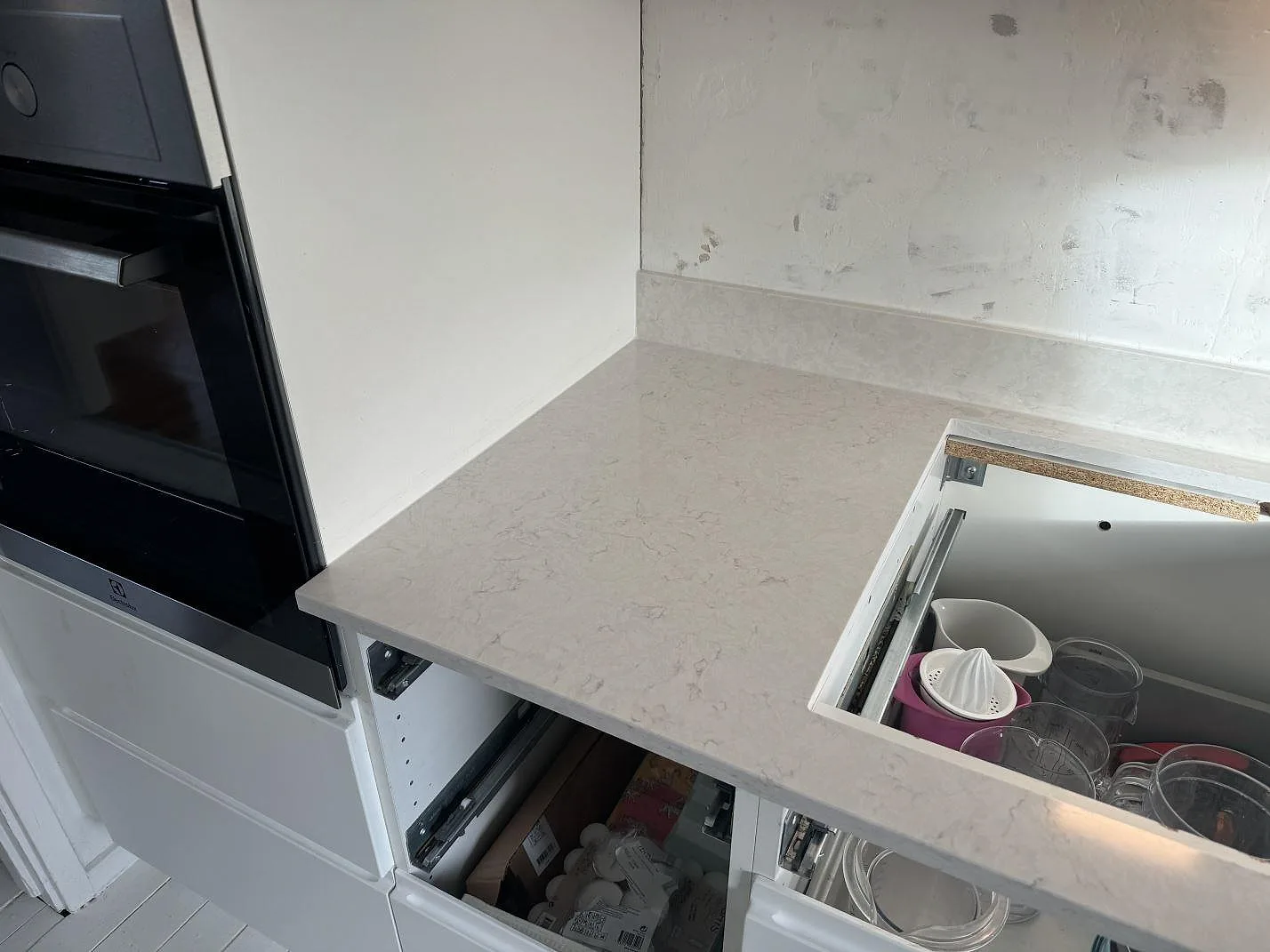 Polerad kompositbänkskiva i Silestone Lagoon bredvid inbyggnadsugn och öppna köksstommar under montering i Pixbo.