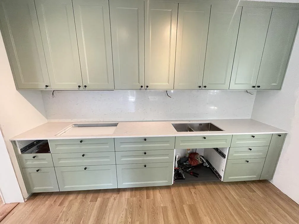 Köksbänkskiva i vit Silestone Lagoon, polerad kvartskomposit, monterad som rak bänk med matchande stänkskydd och underlimmad rostfri diskho i ett kök med salviagröna luckor i Tävelsås.