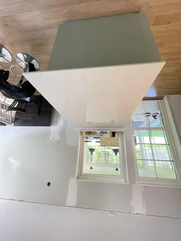 Köksö i vit polerad Silestone Lagoon med salviagrön sida och barstolar i ett kök under montering i Tävelsås.